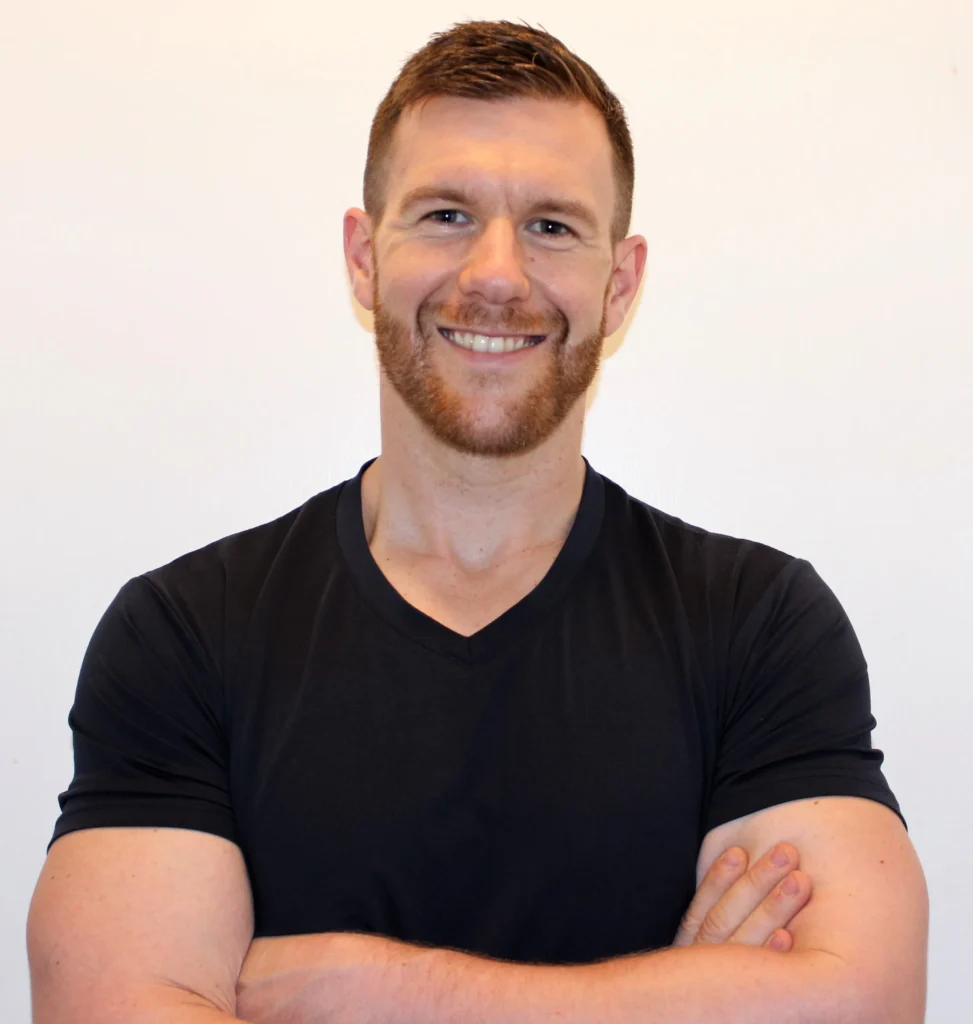 Smiling male fitness trainer standing with arms crossed, ready to guide members at Feel Good Fitness.